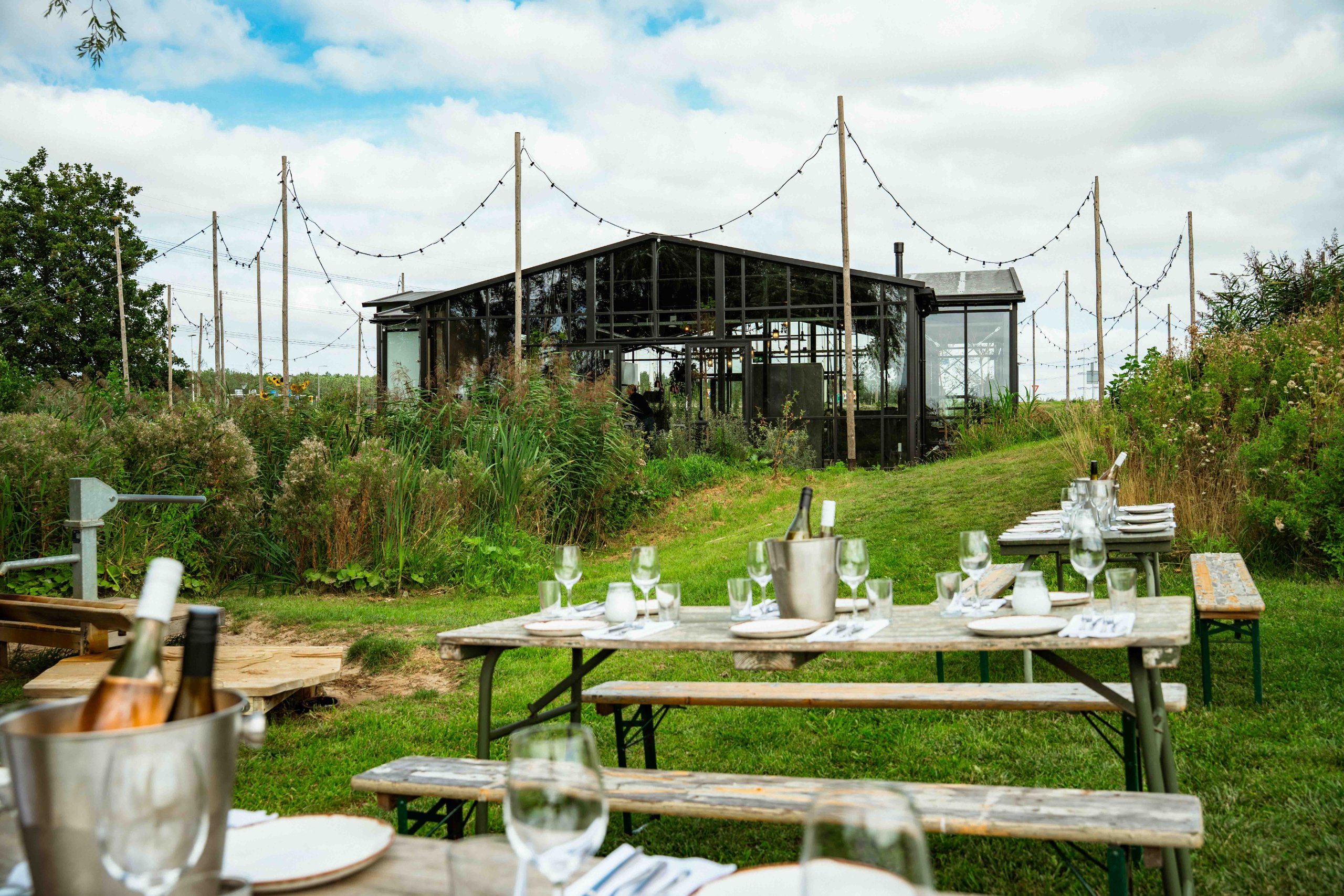 Gedekte picknicktafels in het gras met de glazen kas op de achtergrond bij Brasserie Polderfabriek in Leiderdorp
